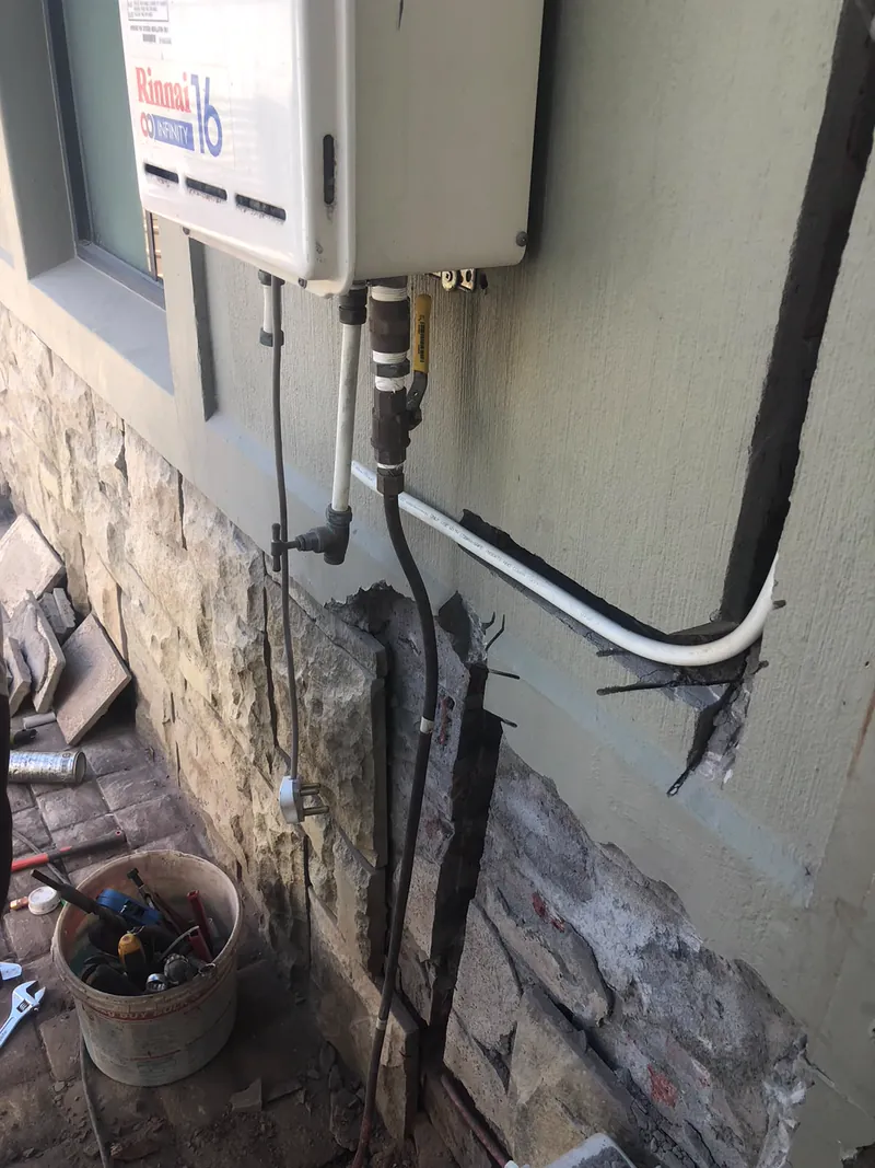 Rinnai gas geyser repair in progress in Cape Town, wall opened up with the gas and water lines exposed and a tool bucket on site